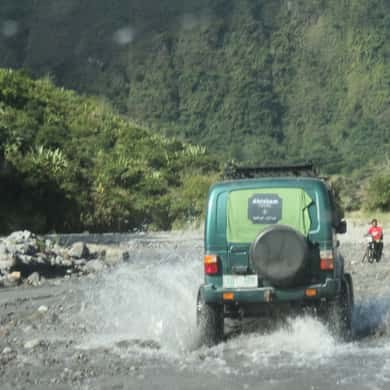 An open-sided 4x4 driving through running water in the riverbed on the way to the trailhead