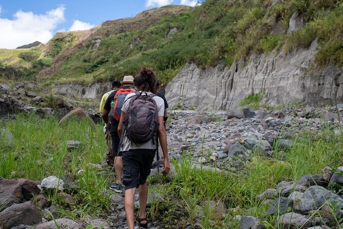 Walkers following the boulder bed of a canyon between banked grey ash walls