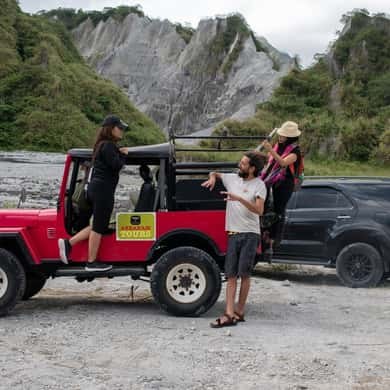 Two vehicles stopped on the ash flat beneath the eroded grey pinnacles of the lahar canyon