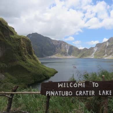 The timber Welcome to Pinatubo Crater Lake sign on the rim path above the water